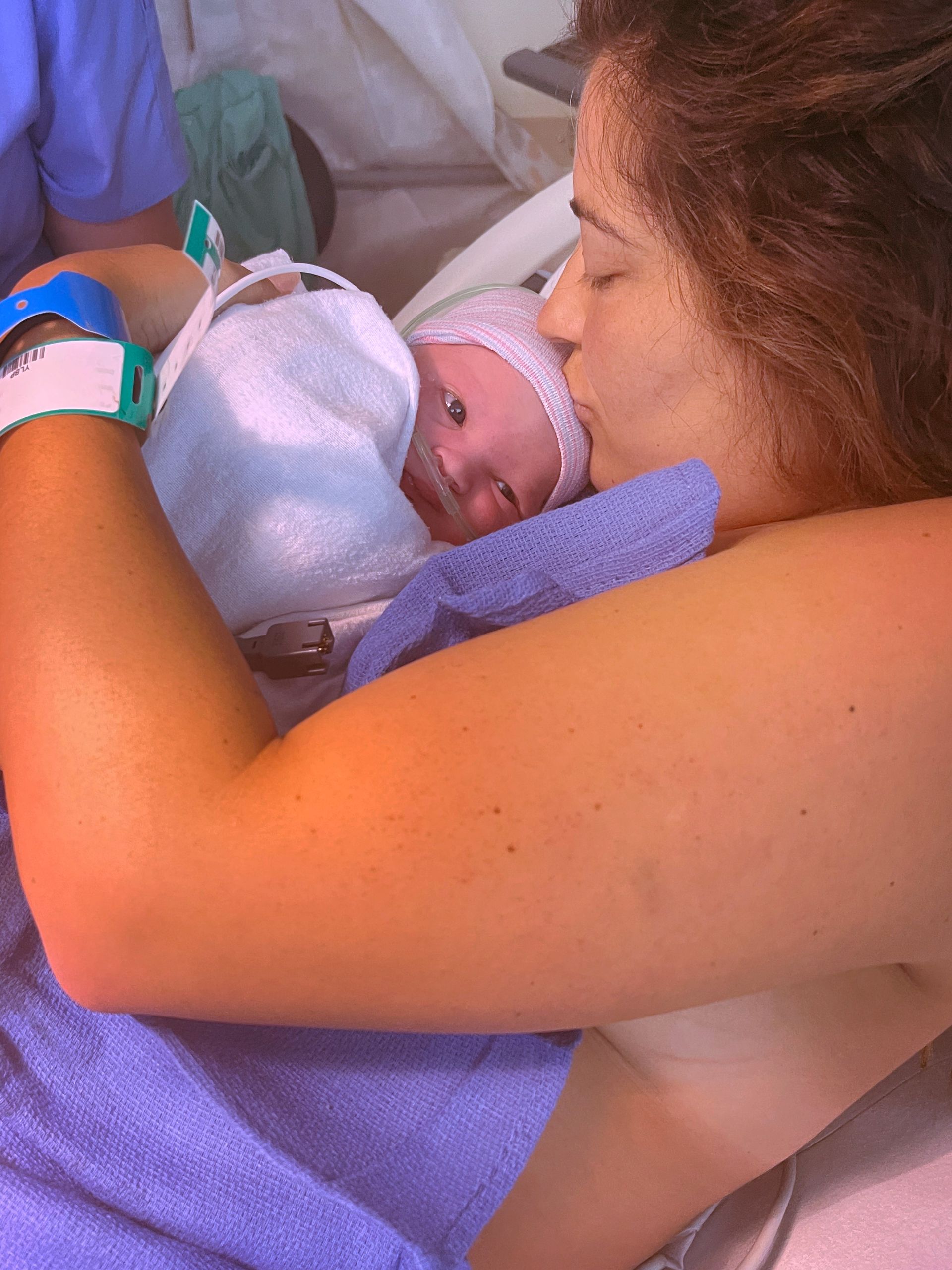 Mother cradling a newborn wrapped in a blue blanket in a hospital bed