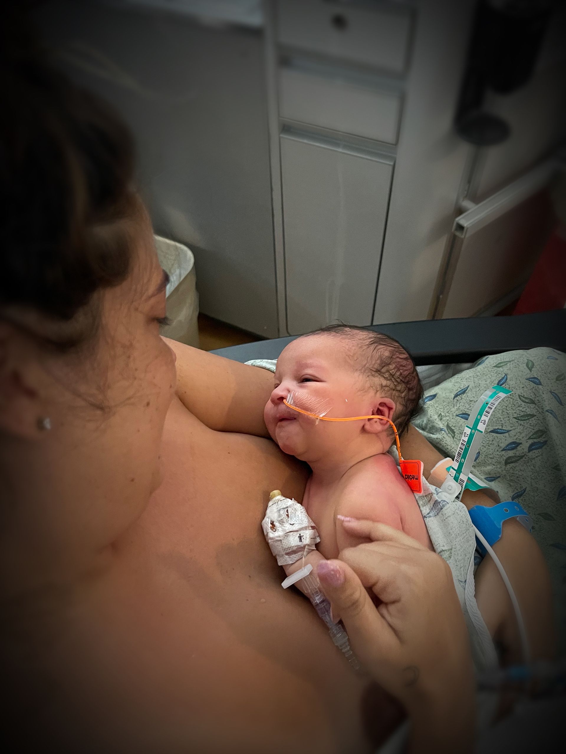 Woman holding a premature baby in a hospital incubator, with medical tubes and monitoring equipment visible