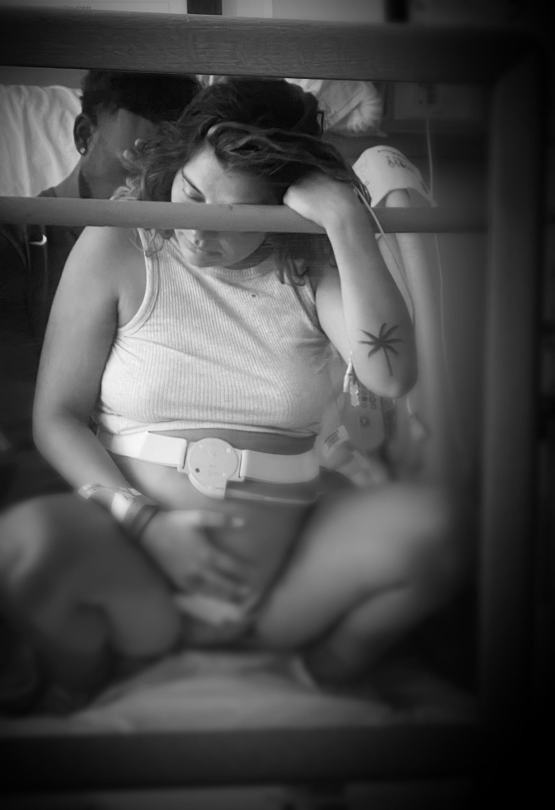 Person seated on a bunk bed, resting head on hand, in a black-and-white photo
