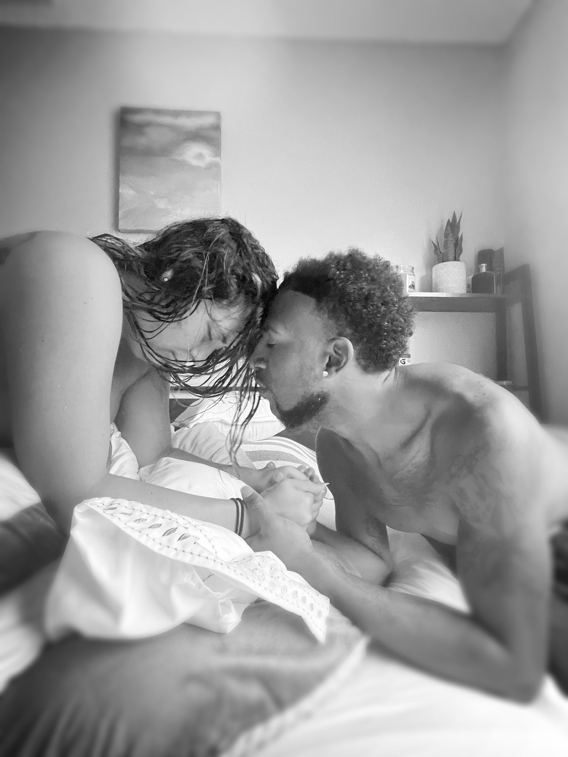 Two people leaning close on a bed in a softly lit bedroom, with one holding papers.