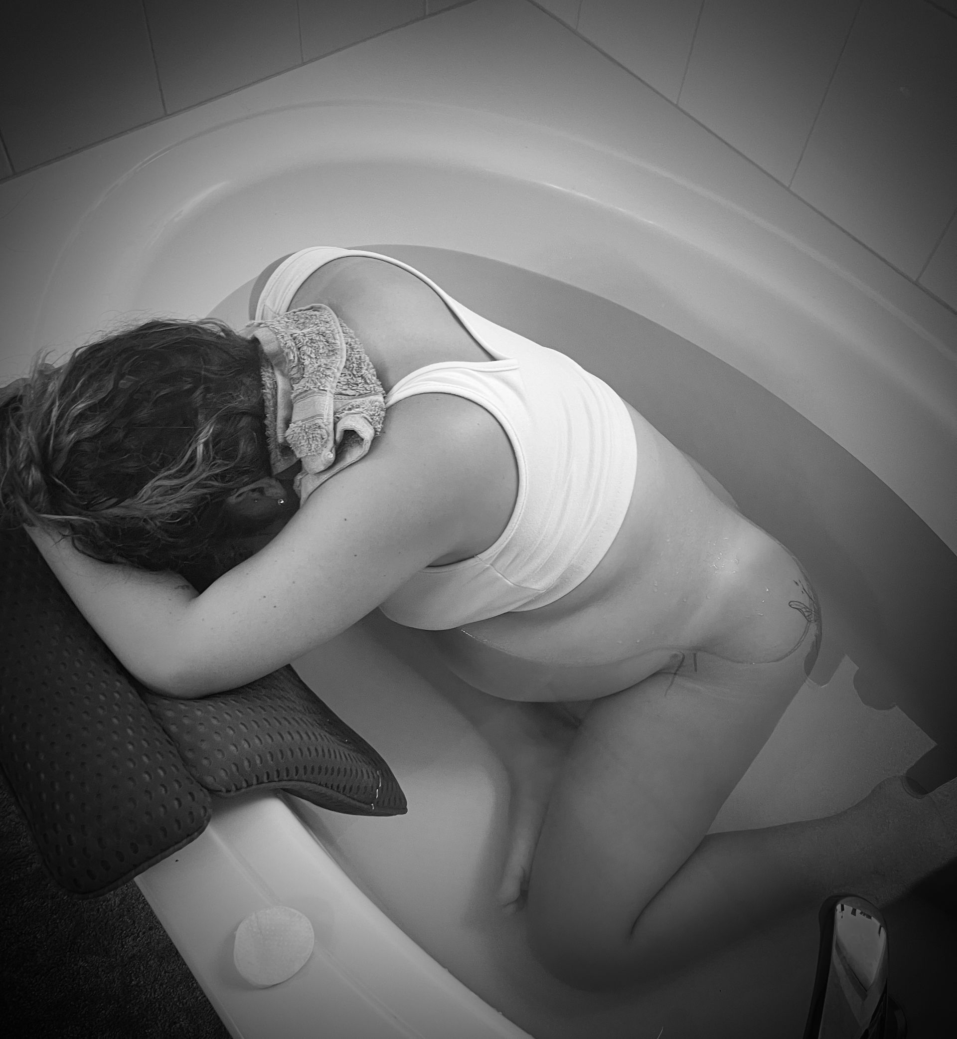 Person curled up asleep in a circular pod, resting on a pillow in dim grayscale lighting